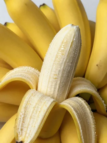 Banane e freskët e plotë dhe e prerë në feta, në tas dhe tavolinë rustike